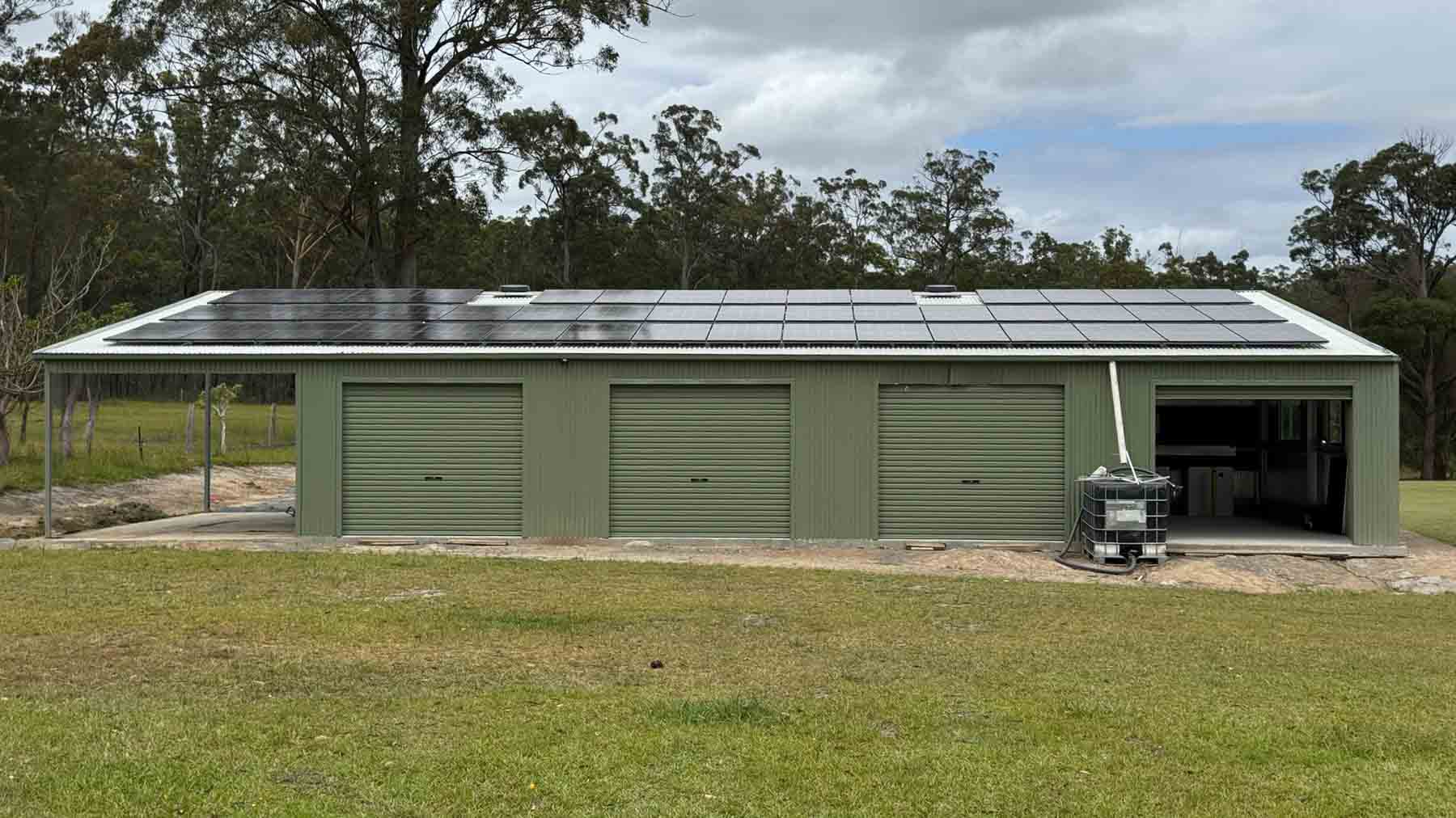 Green farm shed with solar panels on the roof under heavy grey winter cloud